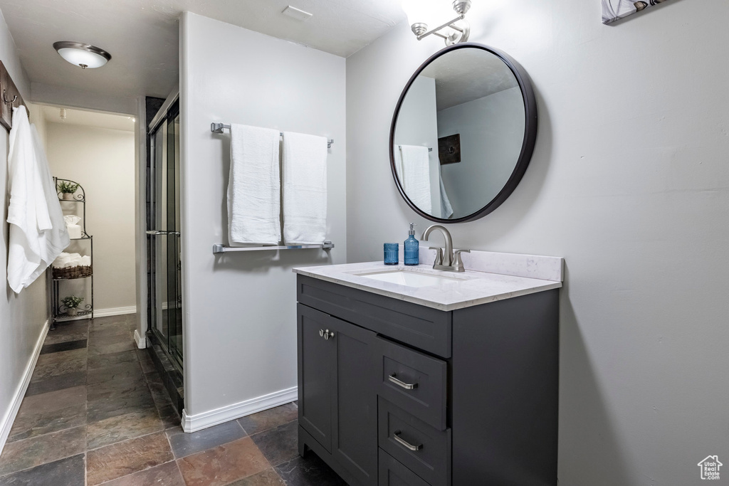 Full bathroom featuring stone tile flooring, vanity, baseboards, and a shower with shower door