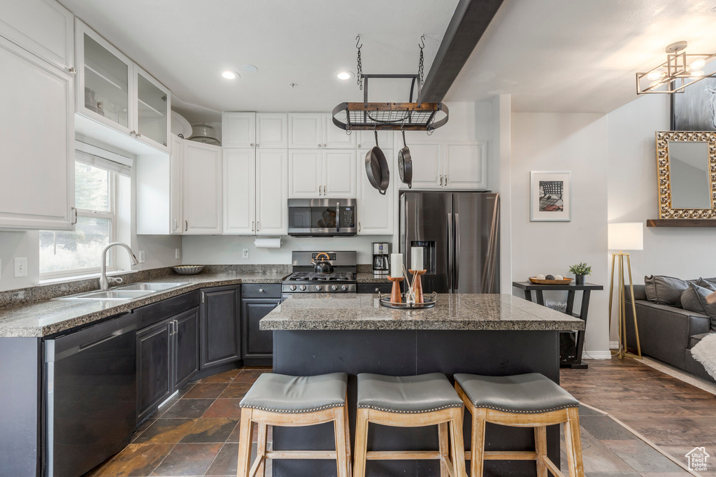 Kitchen featuring appliances with stainless steel finishes, a sink, a breakfast bar area, white cabinets, and a kitchen island