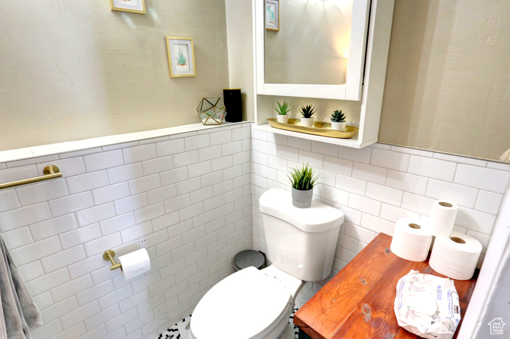 Half bathroom featuring tile walls, wainscoting, and toilet