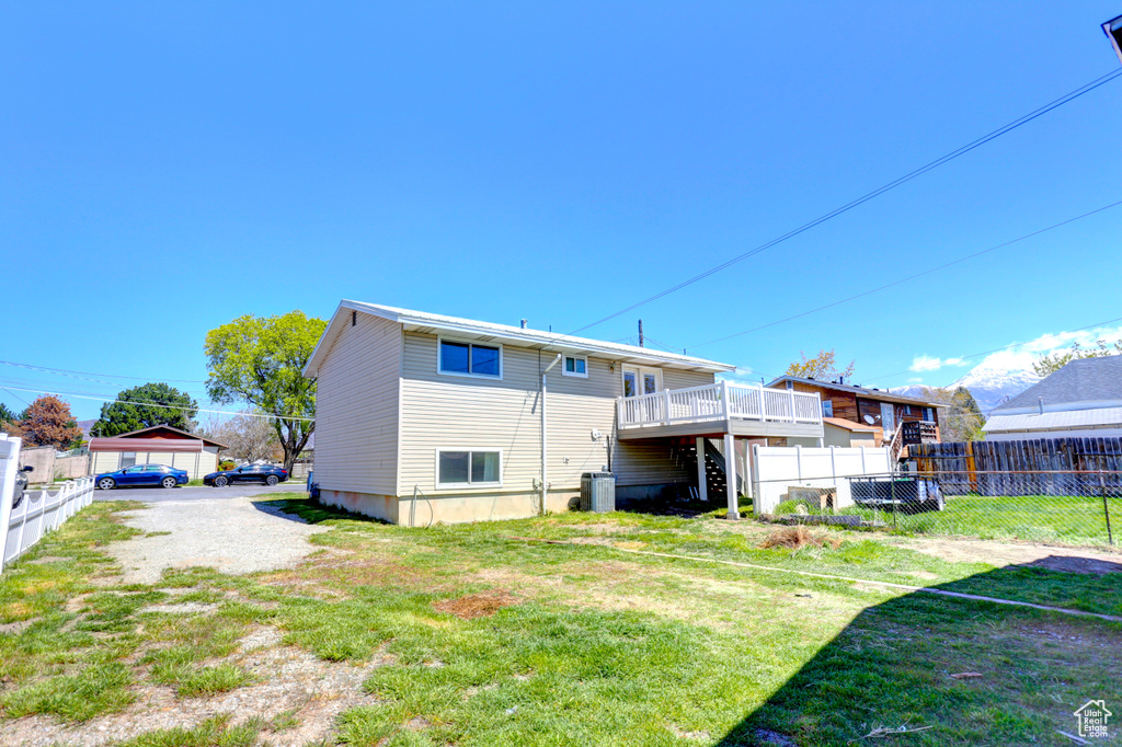 Rear view of property featuring central AC, a wooden deck, fence, and a yard