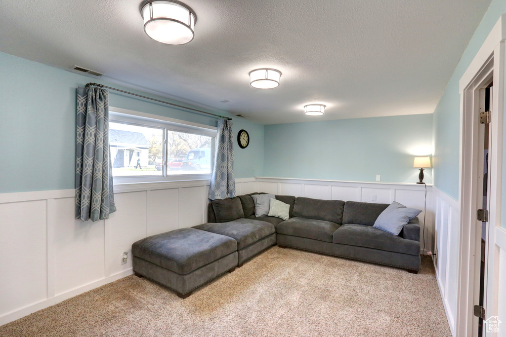 Living area featuring a textured ceiling, visible vents, carpet flooring, and wainscoting