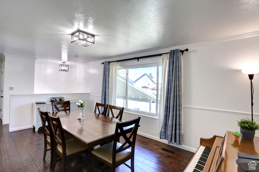 Dining area featuring dark wood finished floors, visible vents, crown molding, and baseboards