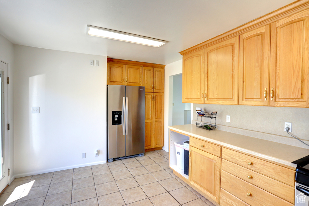 Kitchen with light tile patterned floors, light brown cabinetry, light countertops, and stainless steel fridge