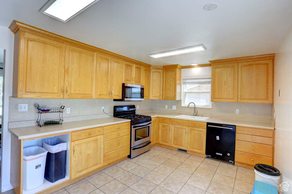 Kitchen with decorative backsplash, appliances with stainless steel finishes, a sink, and light brown cabinetry