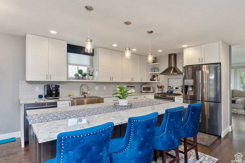 Kitchen with appliances with stainless steel finishes, wall chimney range hood, a toaster, decorative backsplash, and a sink