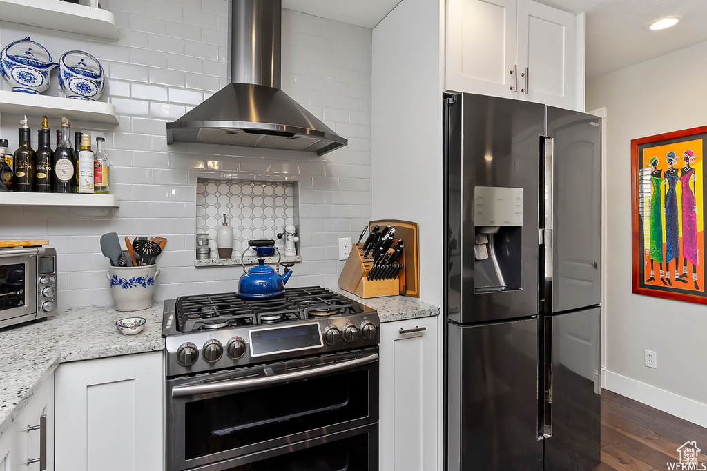 Kitchen with stainless steel appliances, white cabinetry, backsplash, and wall chimney range hood