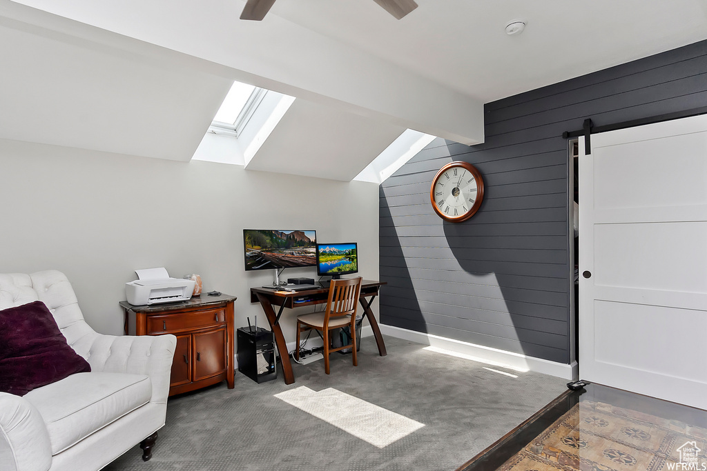 Carpeted office with wood walls, a barn door, and lofted ceiling with skylight