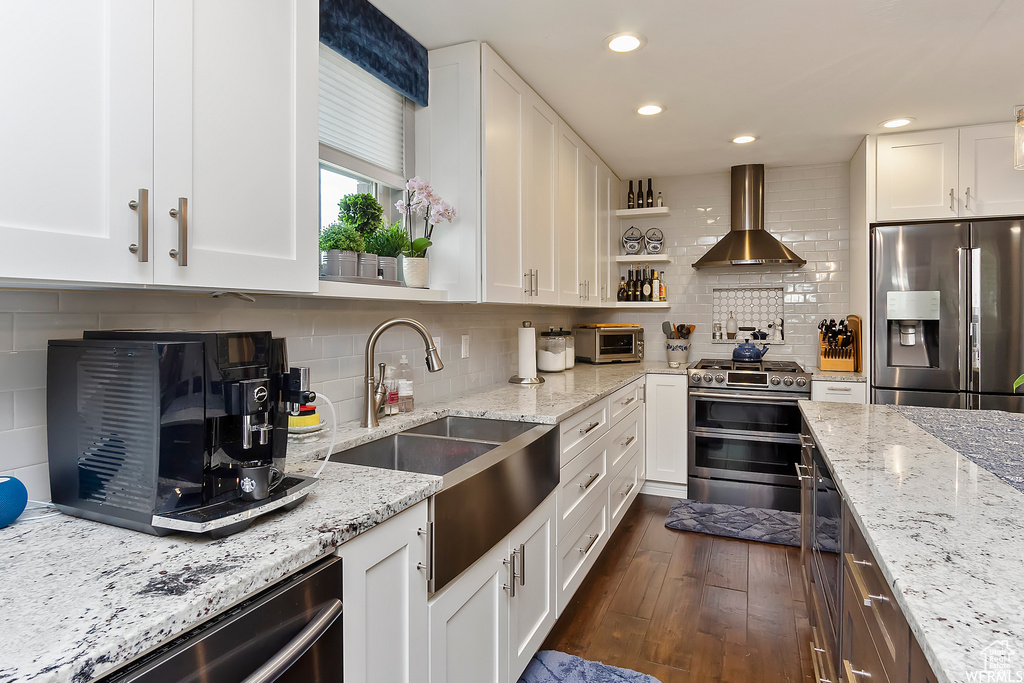 Kitchen with wall chimney range hood, white cabinetry, dark wood-type flooring, stainless steel appliances, and a sink