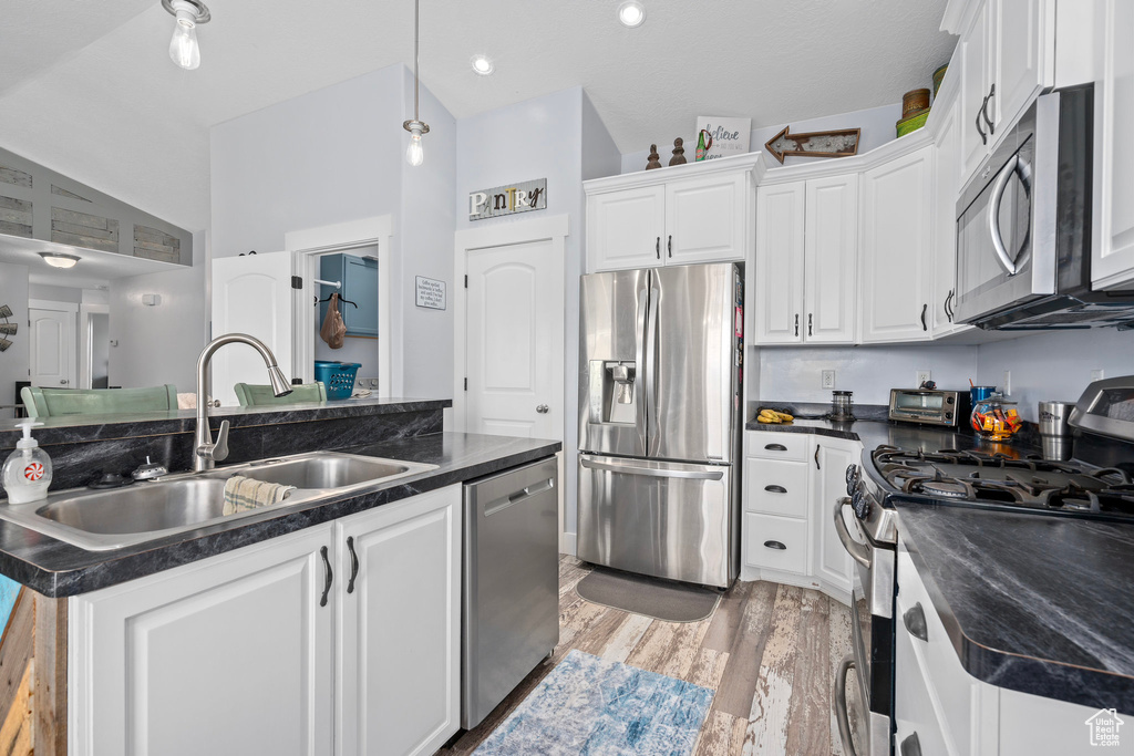 Kitchen featuring stainless steel appliances, light wood finished floors, a sink, and dark countertops