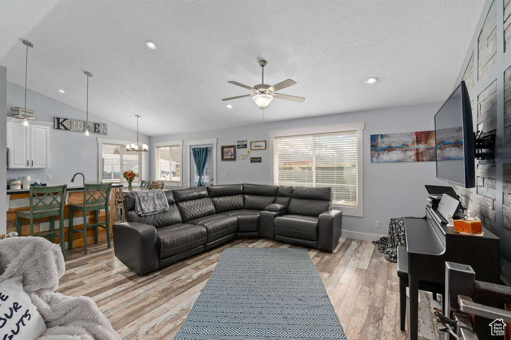 Living room with ceiling fan with notable chandelier, a textured ceiling, recessed lighting, lofted ceiling, and light wood finished floors