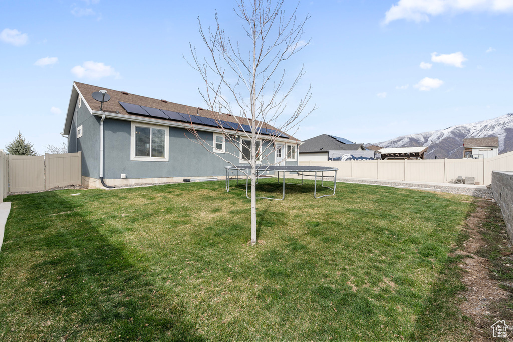 Rear view of house with a trampoline, a fenced backyard, solar panels, and a lawn