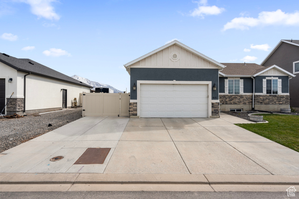View of front of home with driveway, stone siding, board and batten siding, an attached garage, and a gate