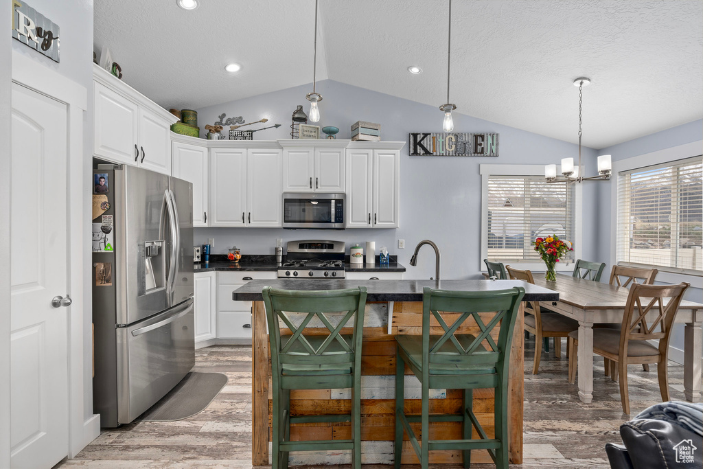 Kitchen with an inviting chandelier, dark countertops, appliances with stainless steel finishes, white cabinetry, and vaulted ceiling