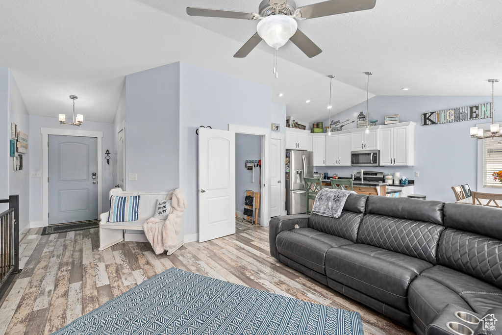 Living room with ceiling fan with notable chandelier, light wood finished floors, and lofted ceiling