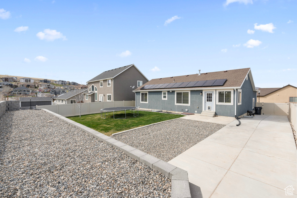 Rear view of house featuring a yard, entry steps, solar panels, a trampoline, and a residential view