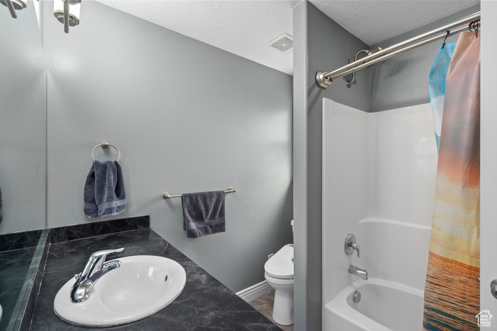 Bathroom featuring a textured ceiling, visible vents, toilet, a sink, and shower / bath combo with shower curtain