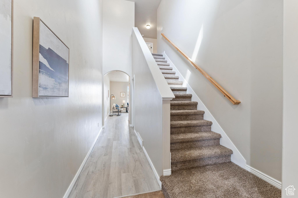 Stairway with arched walkways, wood finished floors, baseboards, and a towering ceiling