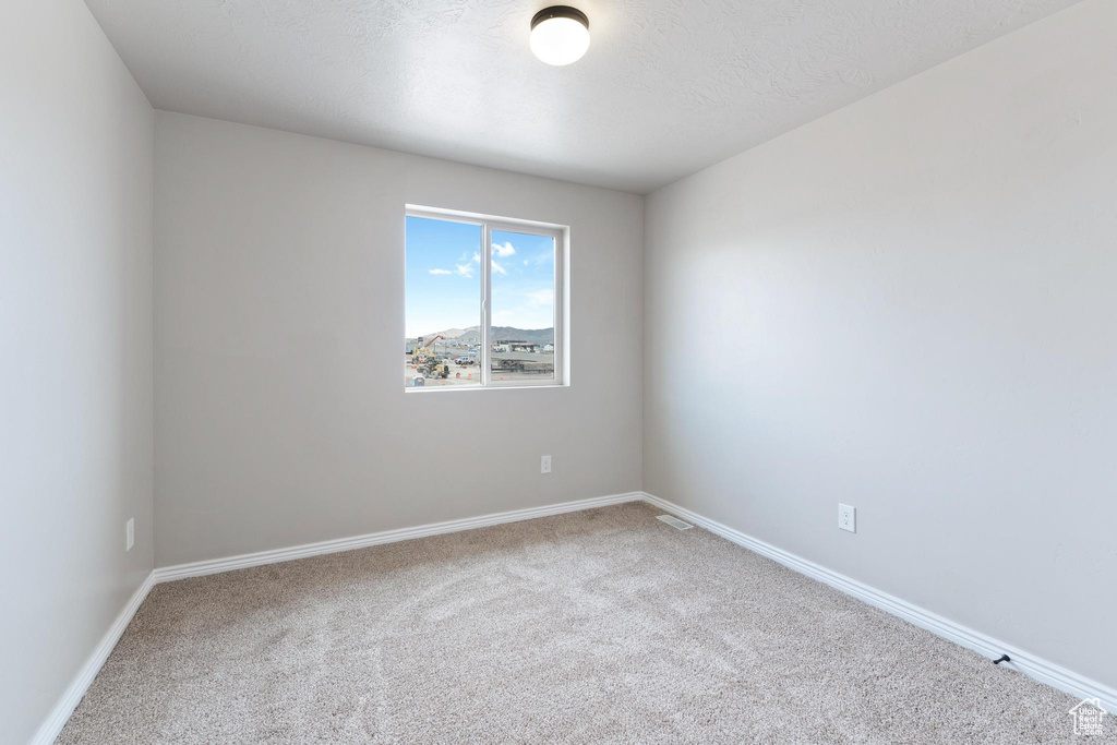 Carpeted empty room featuring a textured ceiling, baseboards, and visible vents