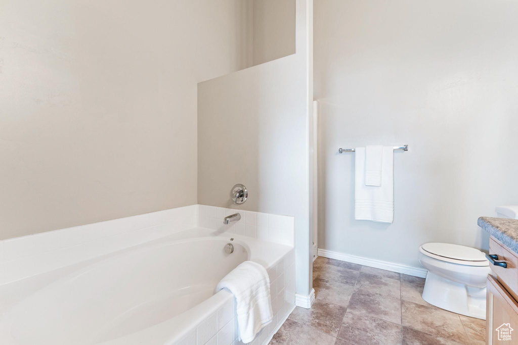 Bathroom with toilet, a bath, vanity, and baseboards