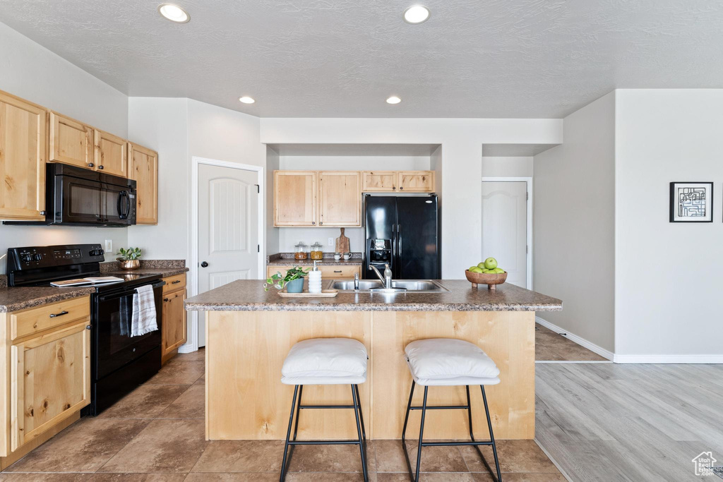Kitchen featuring a breakfast bar, light brown cabinets, black appliances, and dark countertops