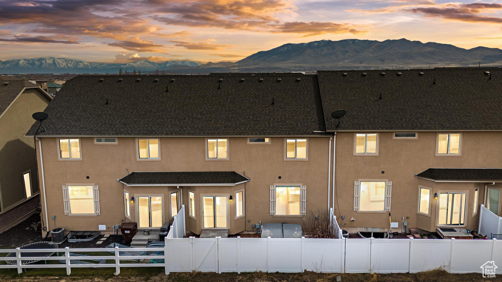 Back of house at dusk featuring roof with shingles, stucco siding, a mountain view, and a fenced front yard
