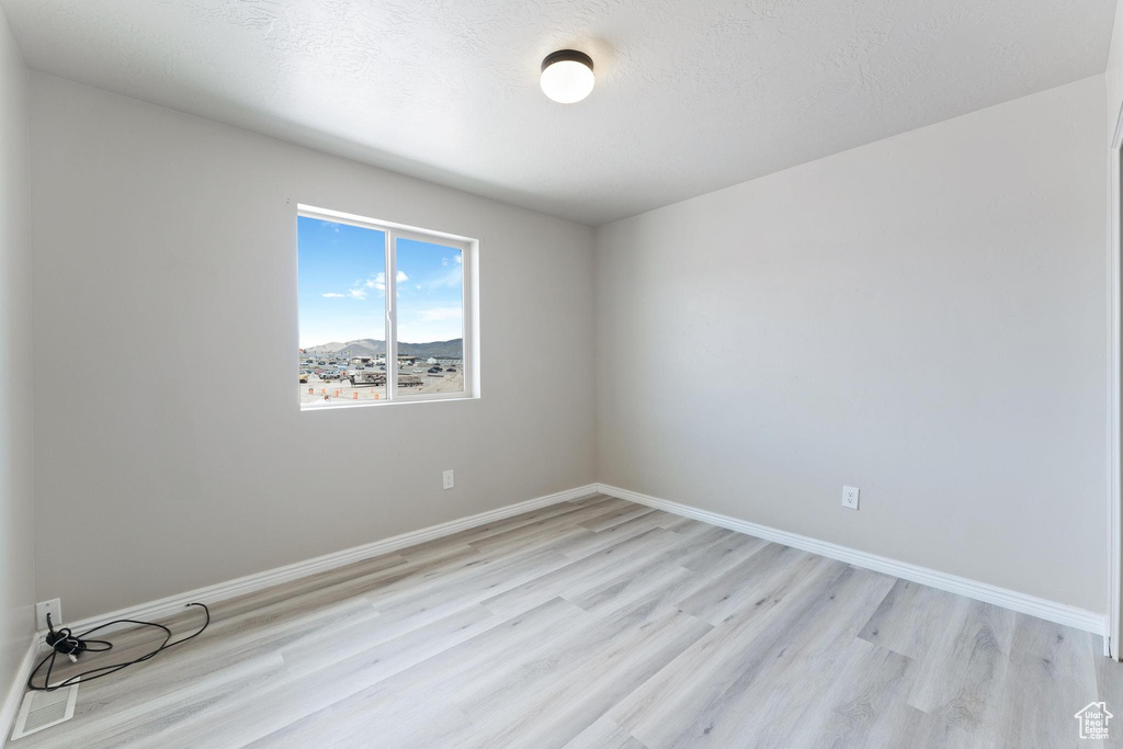 Unfurnished room with a textured ceiling, light wood finished floors, and baseboards