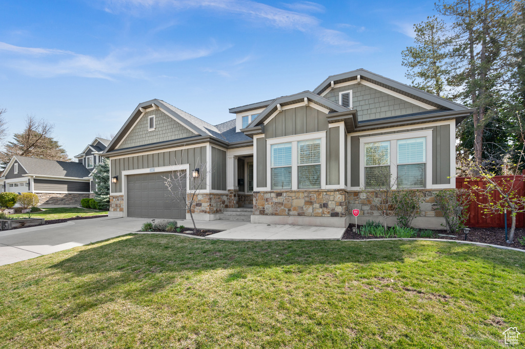 Craftsman house with concrete driveway, board and batten siding, stone siding, a front yard, and a garage