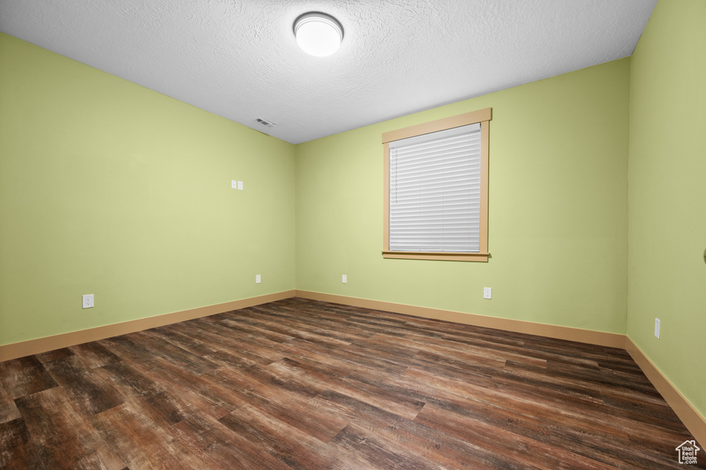 Spare room with dark wood-type flooring, visible vents, baseboards, and a textured ceiling