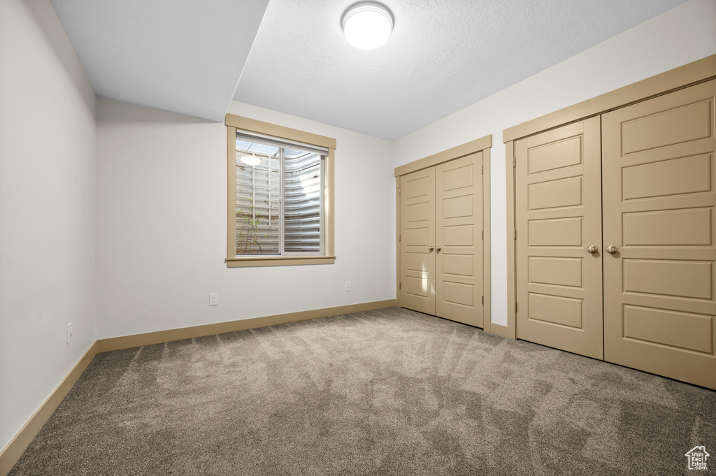Unfurnished bedroom with carpet floors, baseboards, two closets, and a textured ceiling
