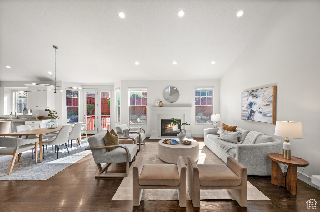 Living room with recessed lighting, dark wood-style floors, a warm lit fireplace, and lofted ceiling