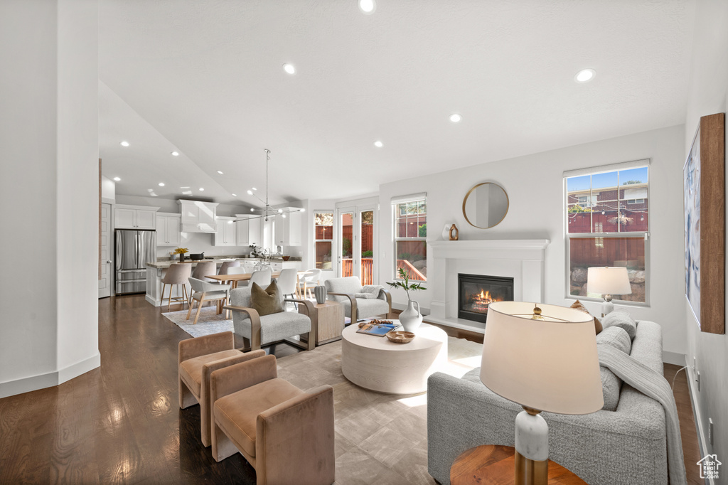Living room with a glass covered fireplace, a healthy amount of sunlight, vaulted ceiling, and dark wood finished floors
