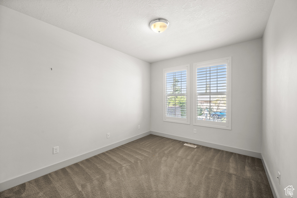 Empty room with carpet flooring, visible vents, baseboards, and a textured ceiling