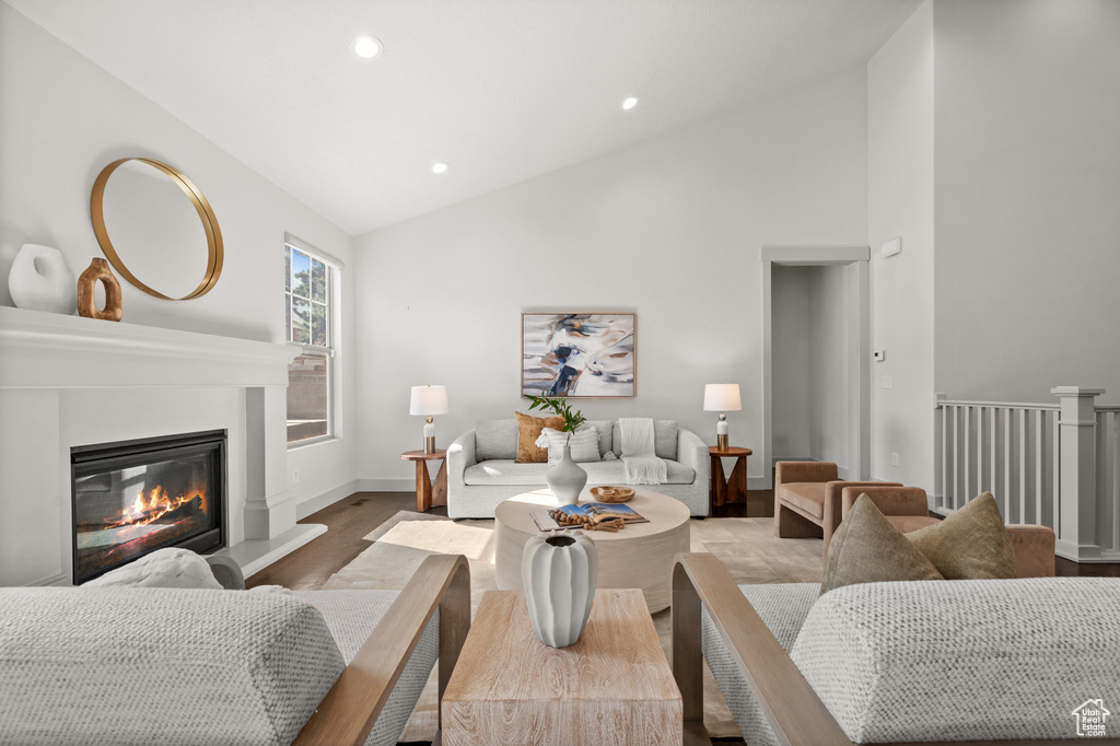 Living room with a glass covered fireplace, baseboards, recessed lighting, high vaulted ceiling, and wood finished floors
