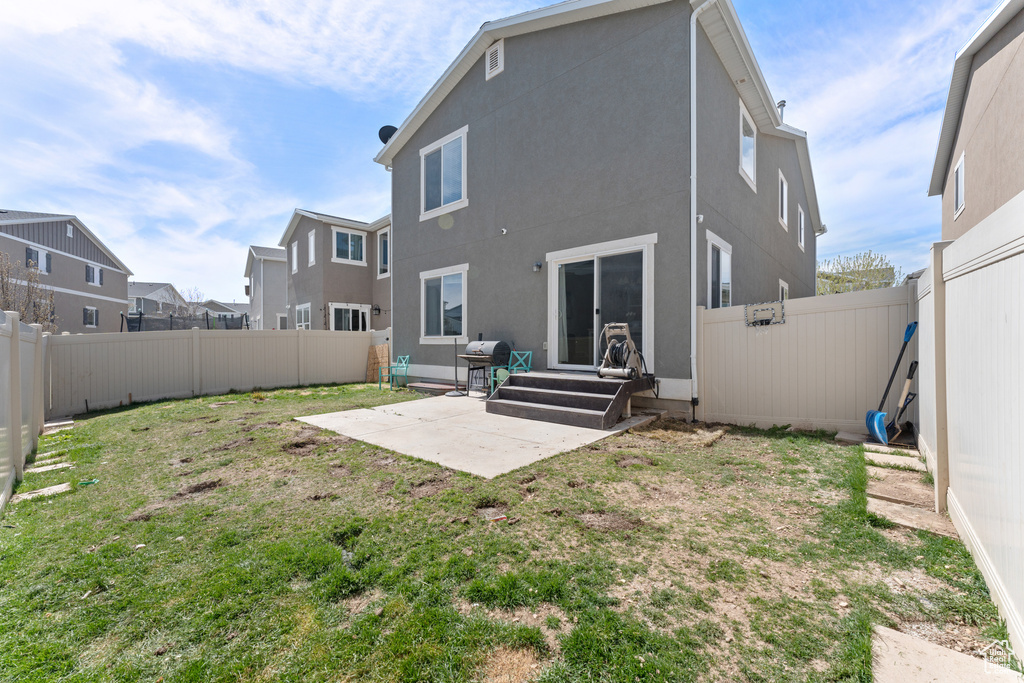 Rear view of property with stucco siding, a patio area, entry steps, a fenced backyard, and a lawn