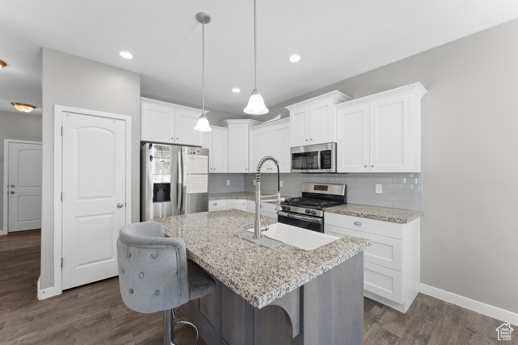 Kitchen featuring tasteful backsplash, white cabinets, appliances with stainless steel finishes, an island with sink, and dark wood-style floors