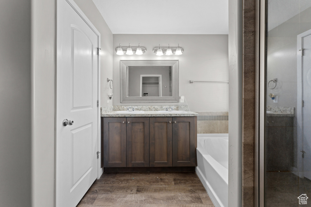 Full bath with a garden tub, wood finished floors, a sink, an enclosed shower, and double vanity