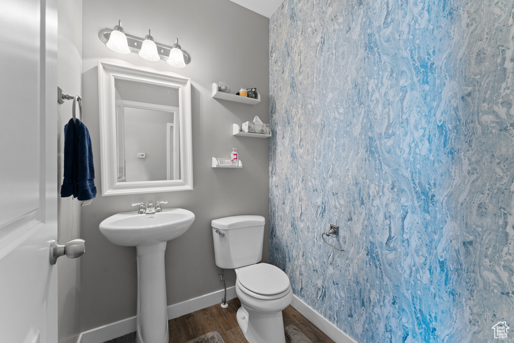 Half bath with toilet, baseboards, wood finished floors, and a sink