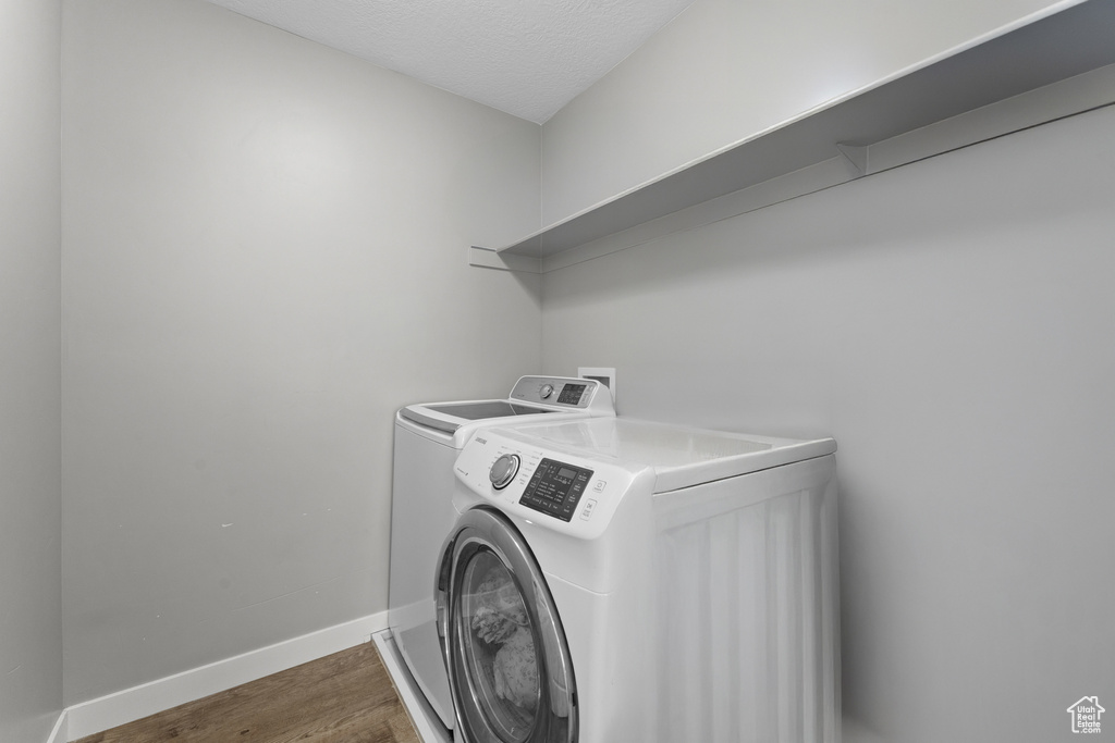 Laundry area featuring laundry area, a textured ceiling, wood finished floors, baseboards, and washing machine and dryer