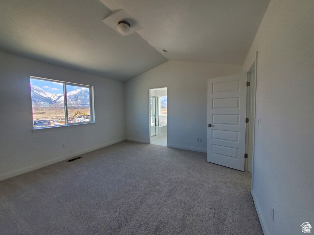 Spare room with a wealth of natural light, visible vents, light carpet, and vaulted ceiling