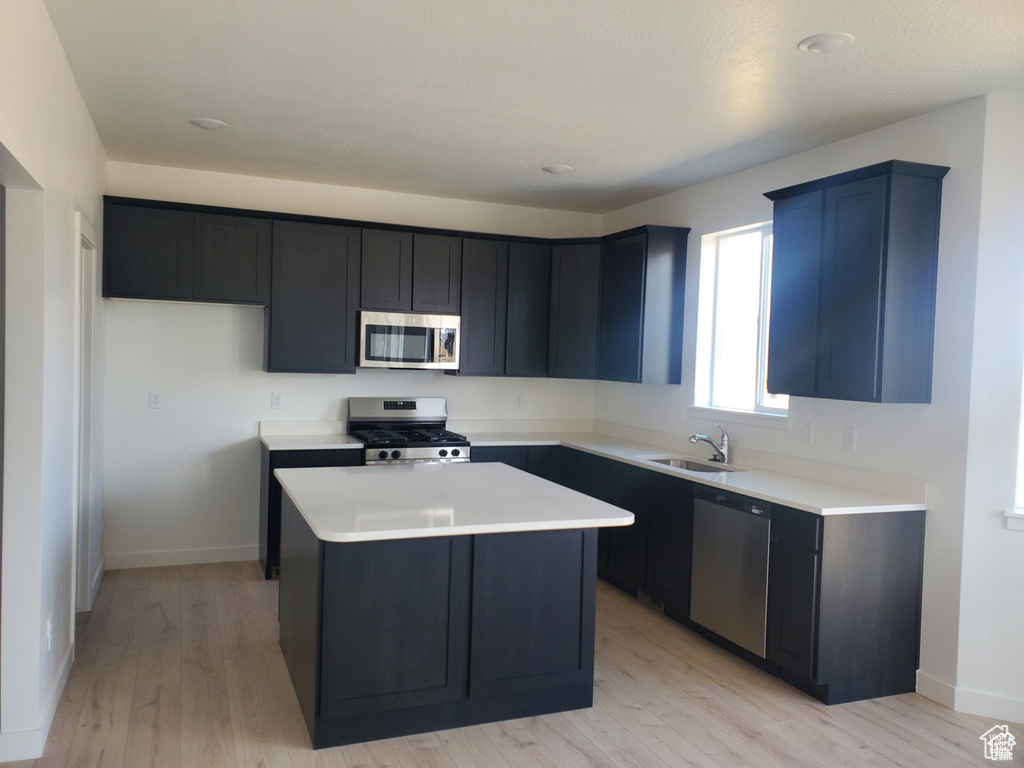 Kitchen with light countertops, a kitchen island, light wood-style floors, appliances with stainless steel finishes, and a sink