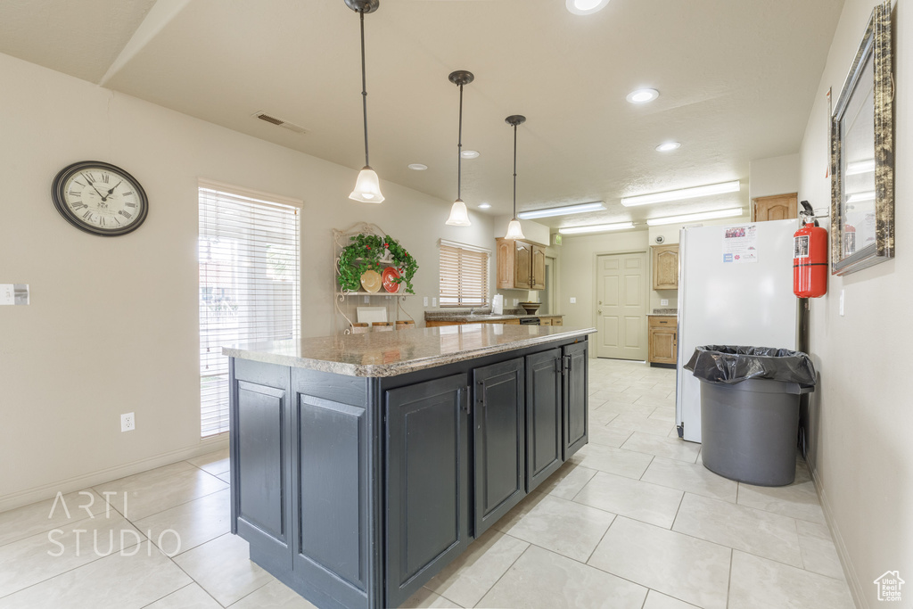Kitchen featuring freestanding refrigerator, visible vents, a center island, light stone counters, and decorative light fixtures