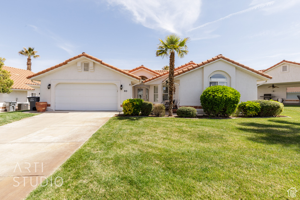 Mediterranean / spanish house with a garage, a front yard, driveway, and stucco siding