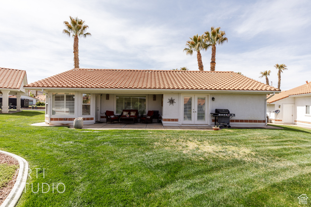 Rear view of property featuring french doors, a tile roof, a patio, and a lawn