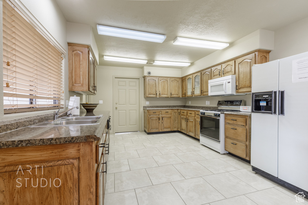 Kitchen with white appliances, glass insert cabinets, a textured ceiling, a sink, and dark countertops