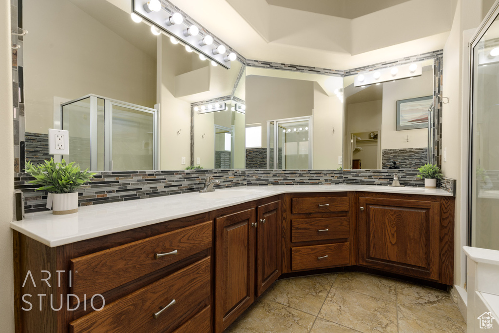 Full bathroom featuring tasteful backsplash, double vanity, a sink, and a stall shower