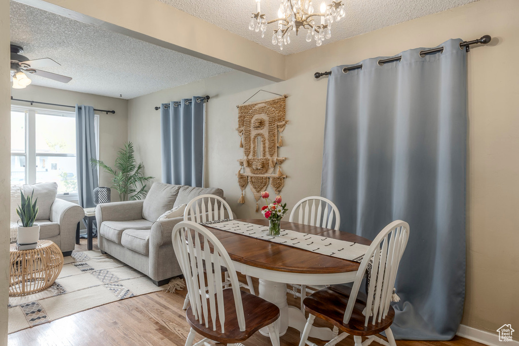 Dining room with a chandelier, a textured ceiling, a ceiling fan, and light wood finished floors