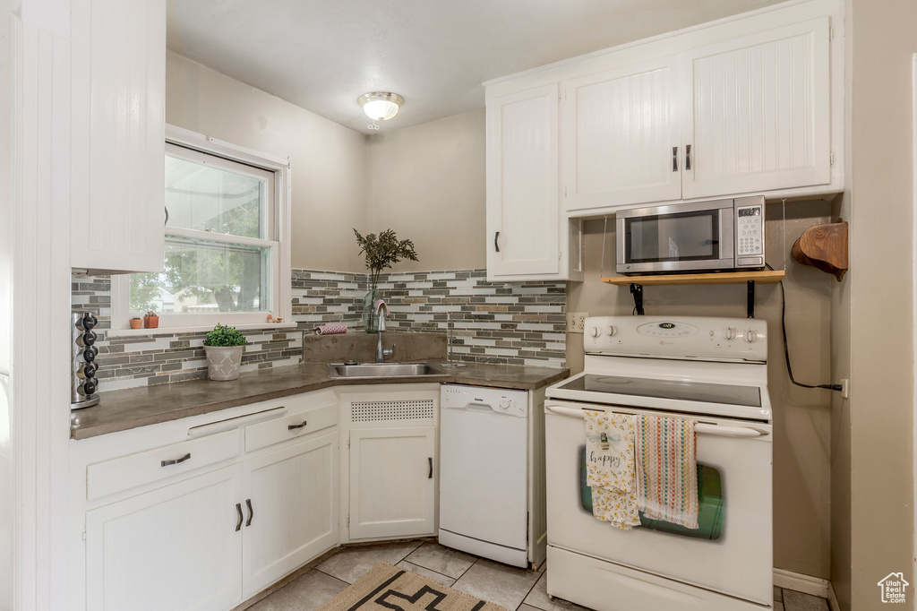 Kitchen featuring white appliances, a sink, tasteful backsplash, and white cabinets