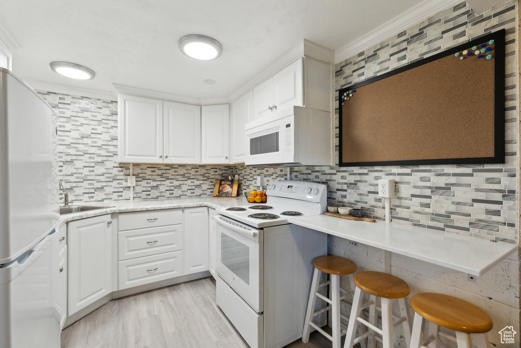 Kitchen with white appliances, light countertops, white cabinetry, decorative backsplash, and ornamental molding