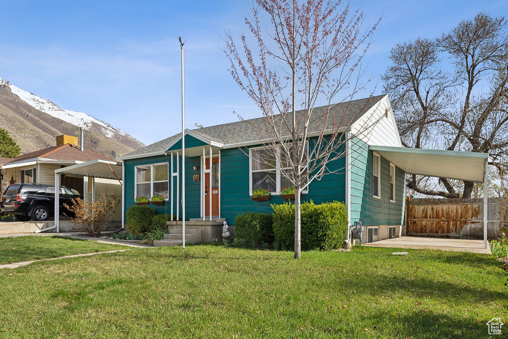 Bungalow-style home featuring a mountain view, a carport, a front yard, fence, and a shingled roof