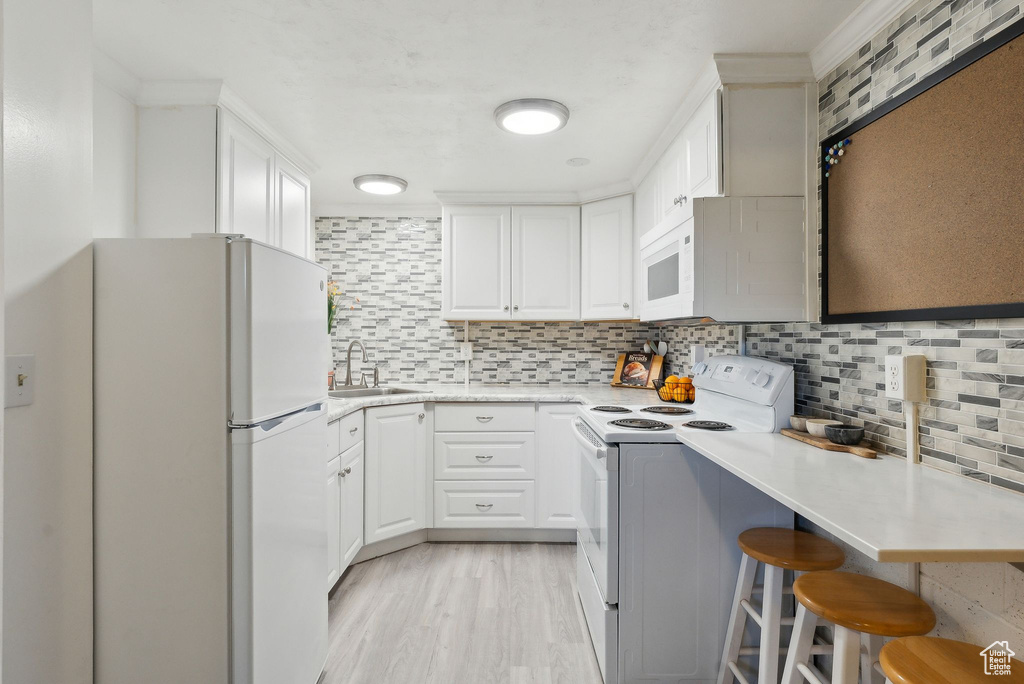 Kitchen featuring tasteful backsplash, white cabinets, a sink, light countertops, and white appliances